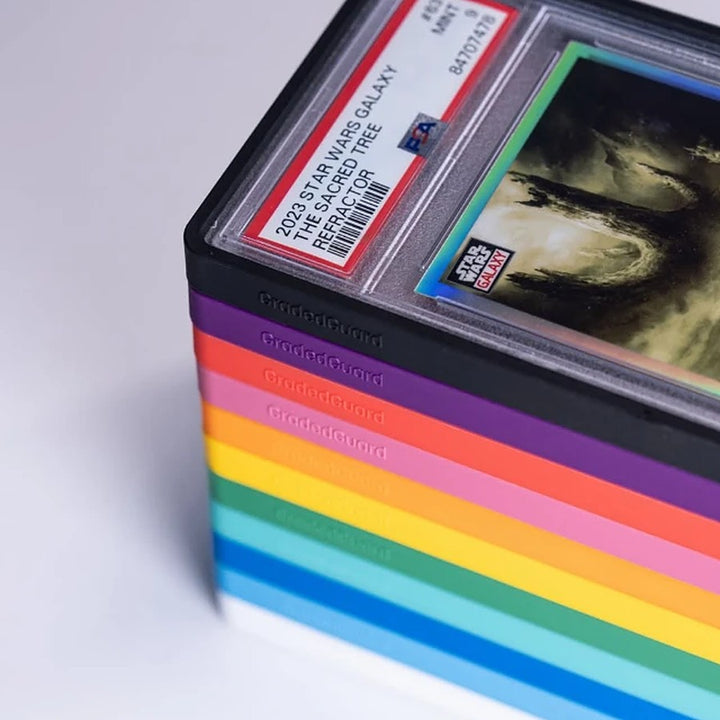 Stapel aus GradedGuard Cases in Regenbogenfarben, zuoberst ein PSA-Slab in schwarzer Case